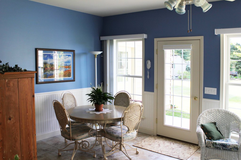 Lovely room with white wainscotting, blue paint, tall windows, glass door to outside, charming cafe table and chairs