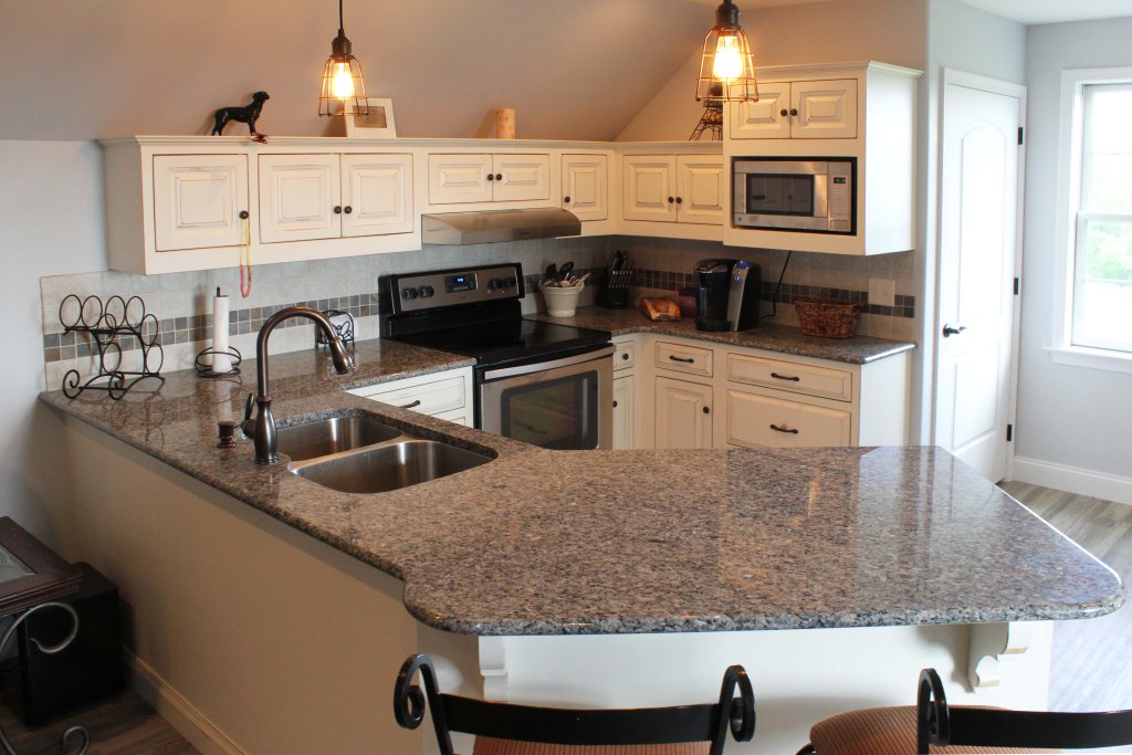 Close up of large kitchen peninsula with double sink and snack bar seating. White kitchen cabinetry, tile backsplash